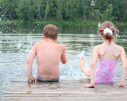 kuvassa laiturilla istuvia lapsia polskimassa jaloillaan veteen.