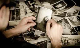 Kuvan henkilö pitää kädessään vanhoja valokuvia.